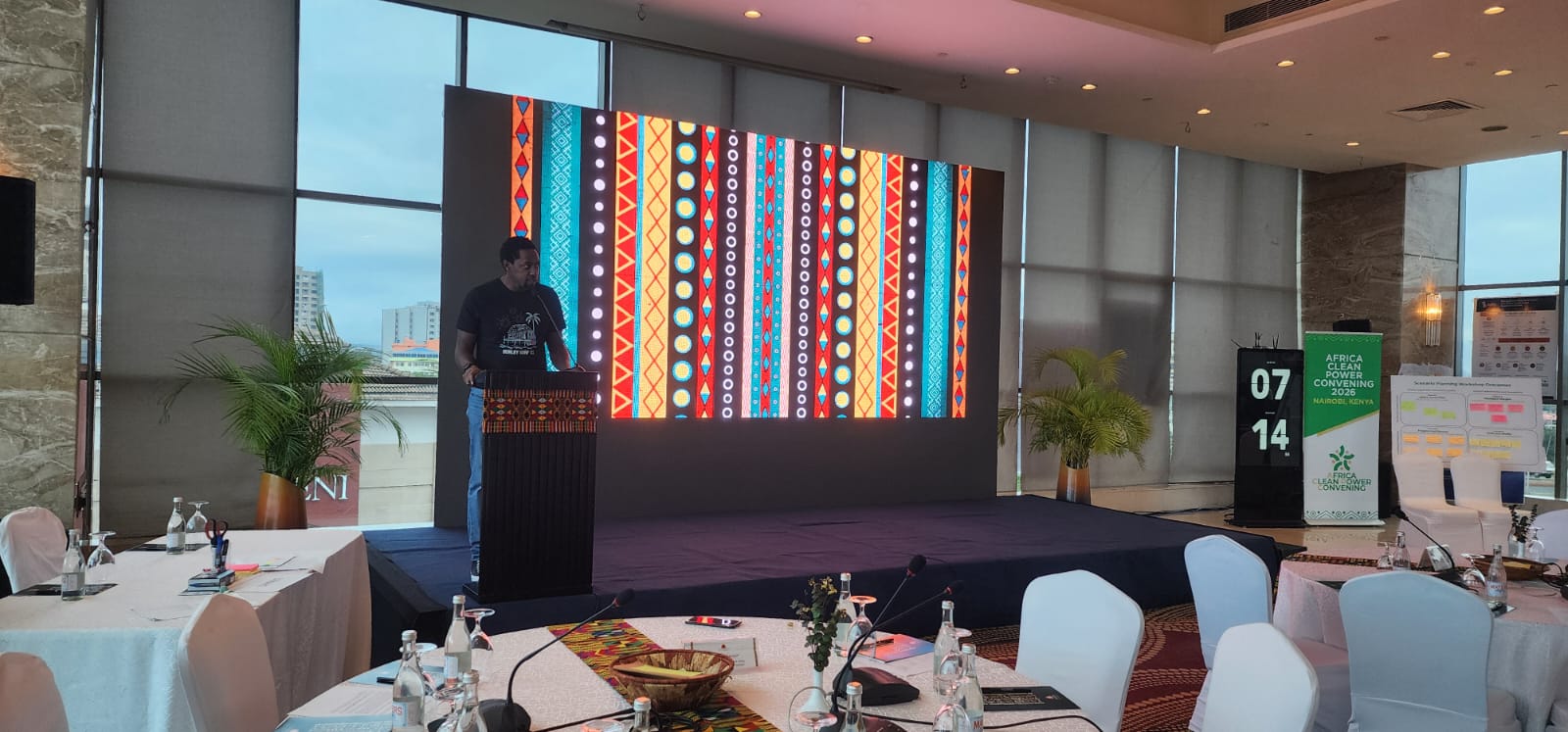 Speaker addressing the Africa Clean Power Convening 2026 with patterned LED backdrop in Kenya