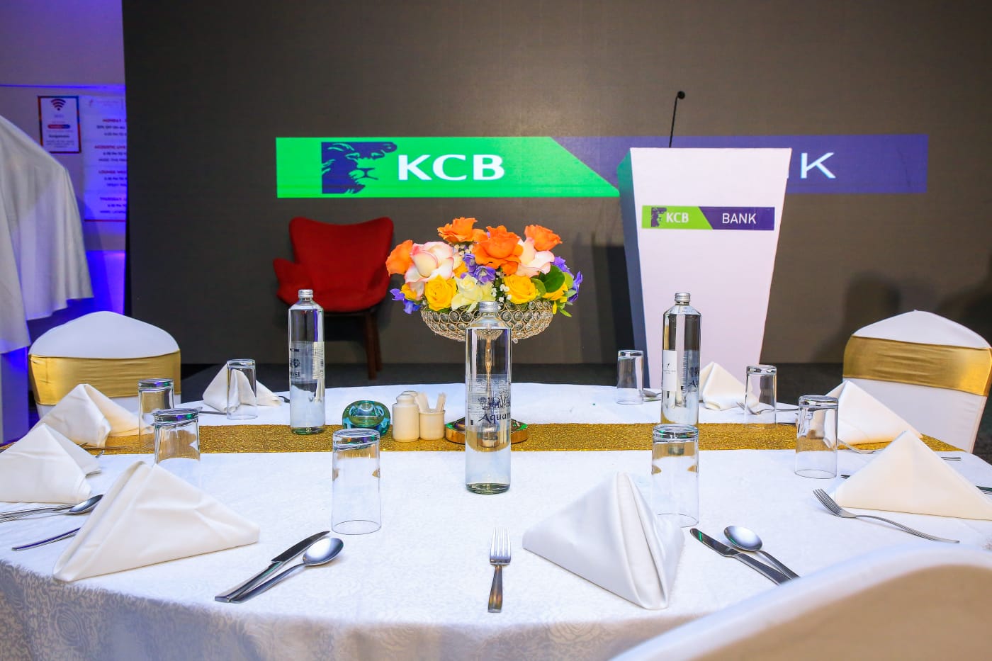 KCB Bank event table setting with floral centrepiece and branded stage backdrop in Nairobi