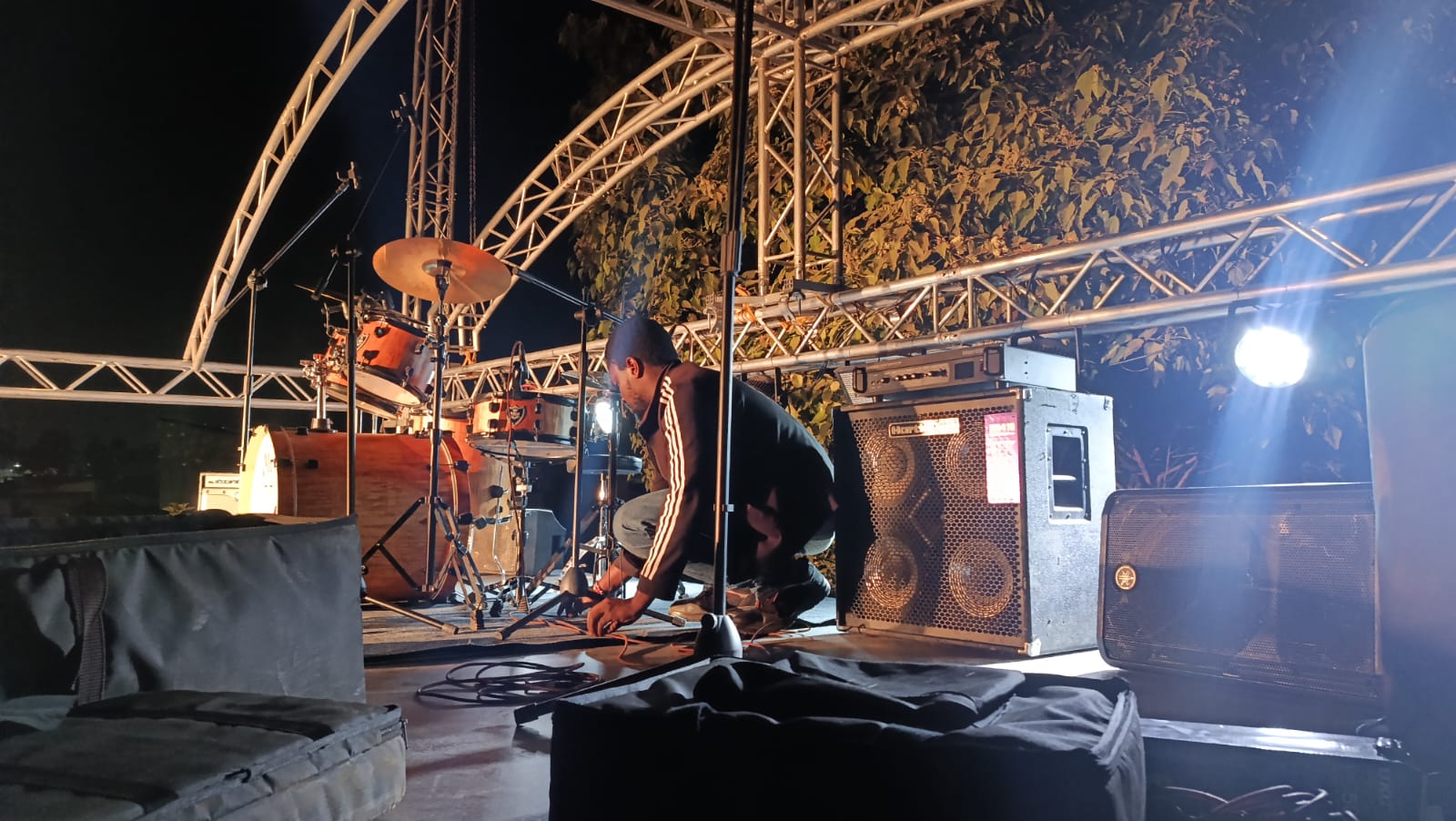 Audio technician preparing microphones and backline on an outdoor truss stage at night in Kenya